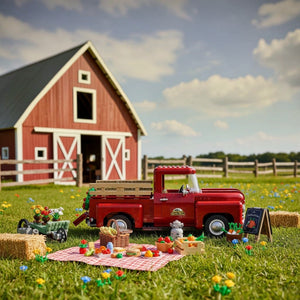 Red toy truck with picnic setup in front of a red barn on a grassy field.