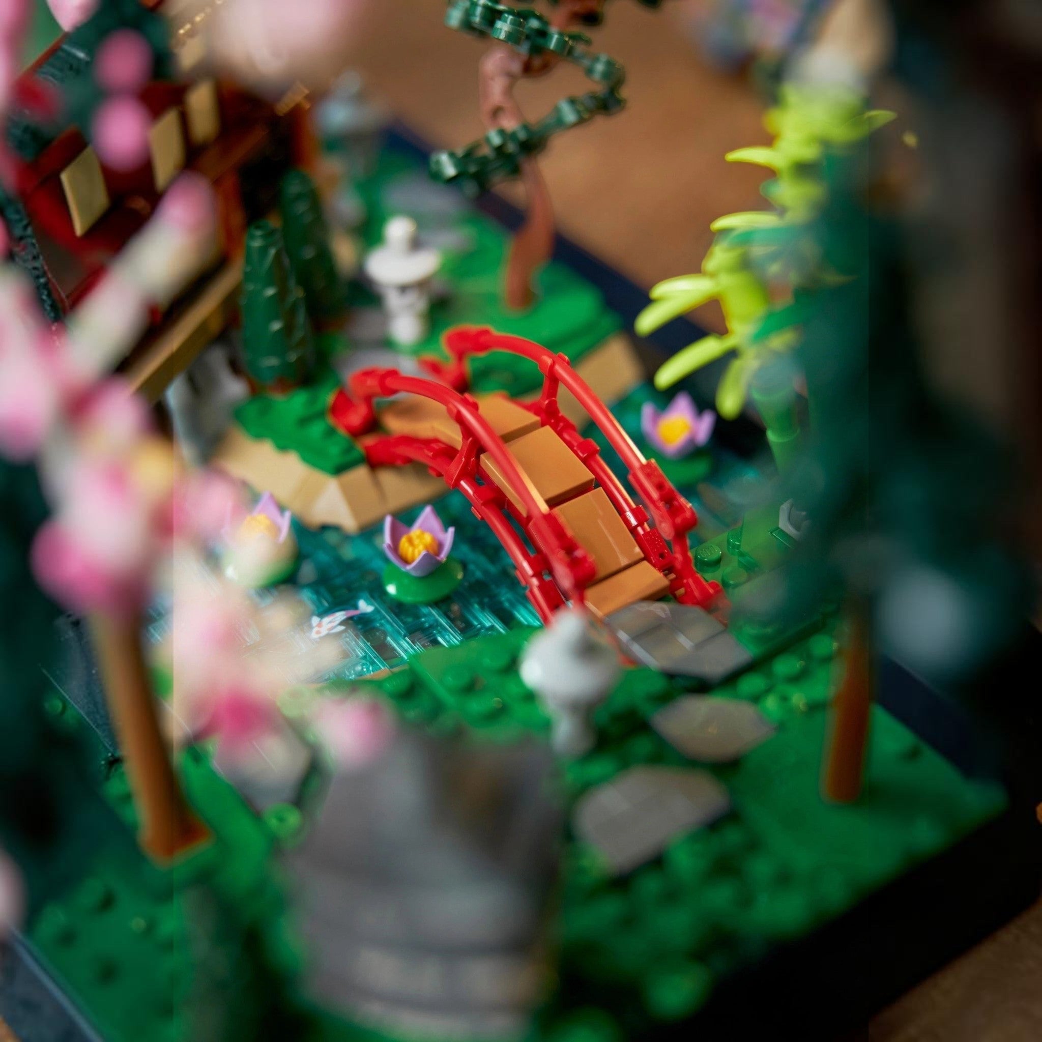 Close-up of a LEGO model with a red bridge, green trees, and small figures on a blurred background.