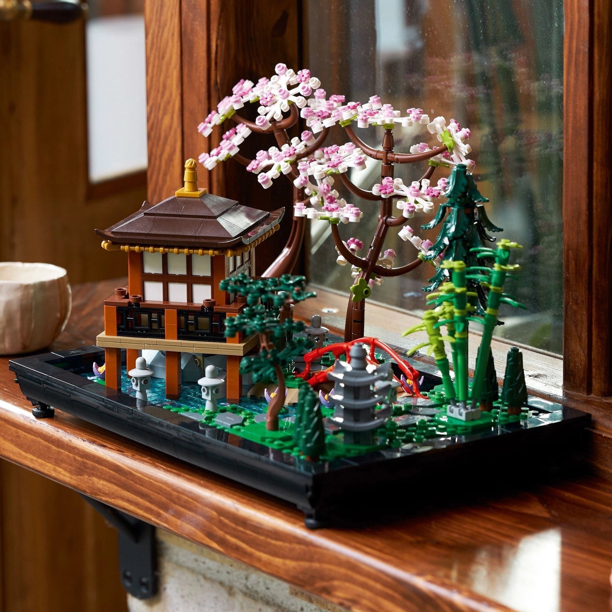 Model of a Japanese temple with cherry blossom tree and fountain on a wooden surface.