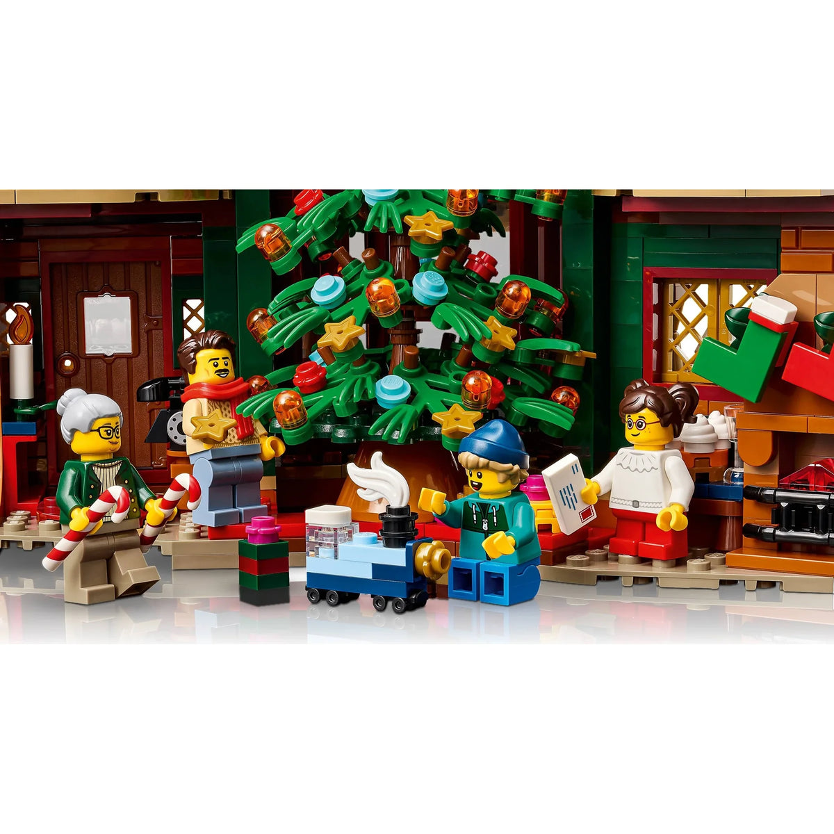 [built-detail] LEGO minifigures arranged around a decorated Christmas tree in a holiday village scene, with gift boxes and a house setting visible in the background.