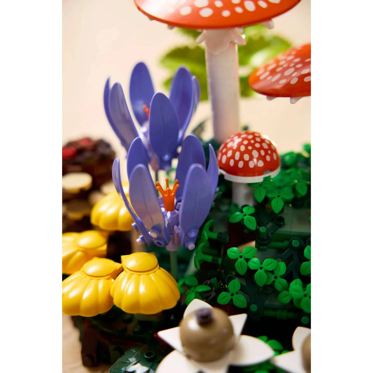 [lifestyle-person] Toy set with purple flower, yellow mushrooms, and red mushroom with white spots on a white background