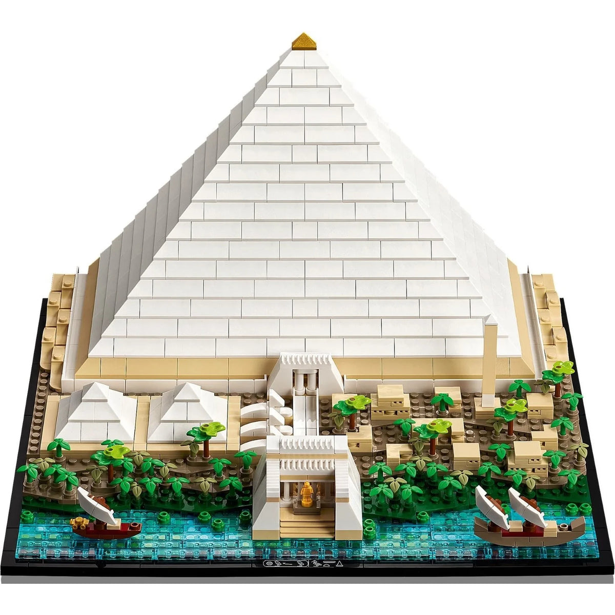 [built-angle] A detailed brick-built model of the Great Pyramid of Giza, featuring a large white brick pyramid, beige sandstone base, green palm trees, blue water, and small toy boats, shown on a plain white background.