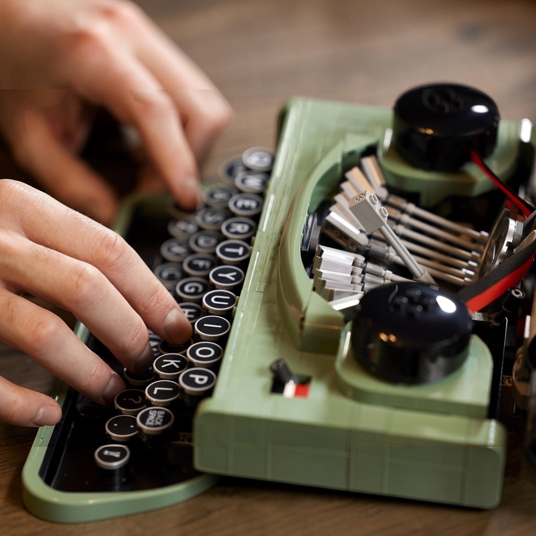 Person typing on a vintage green typewriter with close-up focus on hands and keys.