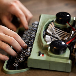 Person typing on a vintage green typewriter with close-up focus on hands and keys.