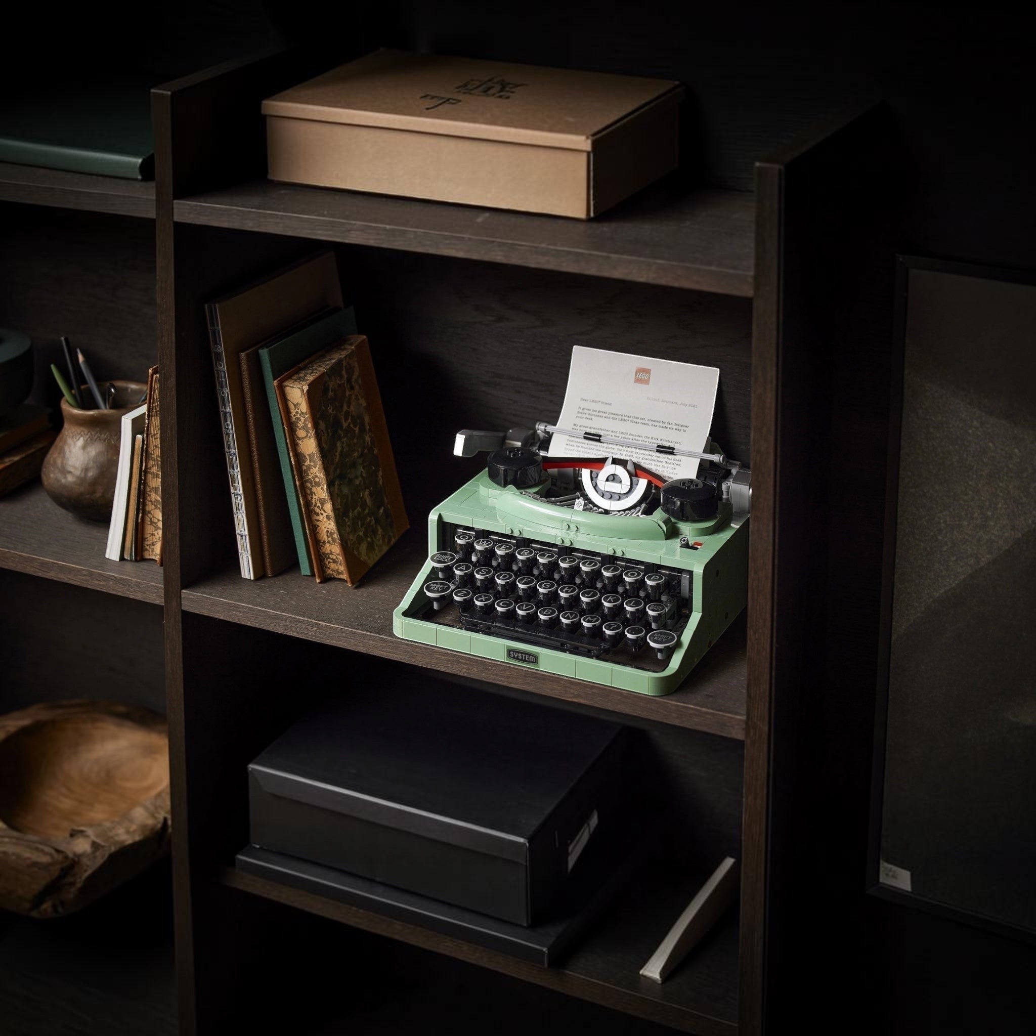 Vintage-style green typewriter on a wooden shelf with books and a box.
