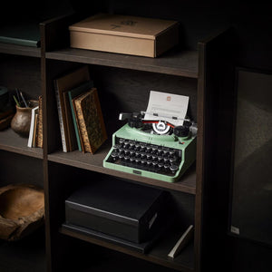 Vintage-style green typewriter on a wooden shelf with books and a box.