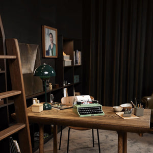 Vintage green typewriter on a wooden desk with bookshelves and decor in the background
