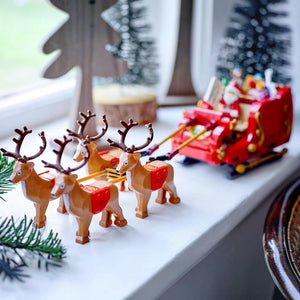 Toy reindeer pulling a toy sleigh with Santa Claus on a windowsill.