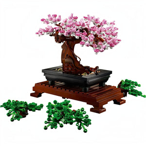 A Brick Apart LEGO Bonsai Tree model with pink cherry blossoms, rectangular pot, and wooden stand with extra green leaves.