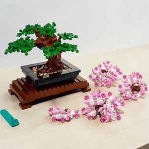 A Brick Apart LEGO Bonsai Tree set with green leaves, interchangeable pink cherry blossoms, and a wooden display stand.