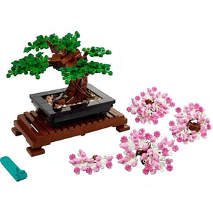 A Brick Apart LEGO Bonsai Tree set with interchangeable green leaves and pink cherry blossom crowns on a wooden stand.