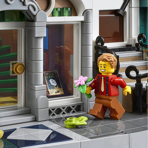 A Brick Apart LEGO Creator Expert Bookshop minifigure holding a pink flower in front of the detailed storefront.