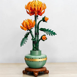 A Brick Apart LEGO Icons Chrysanthemum set featuring a vibrant orange flower in a pastel-green pot on a wooden plinth.