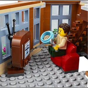 A Brick Apart LEGO Creator Expert Corner Garage apartment interior with a minifigure eating on a red sofa watching TV.