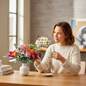 A Brick Apart LEGO Botanicals Pretty Pink Flower Bouquet in a white vase on a table with a woman drinking coffee.