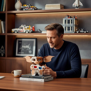 A Brick Apart LEGO Ideas Gizmo figure with 3D glasses sitting on a desk in front of a man in a home office setting.
