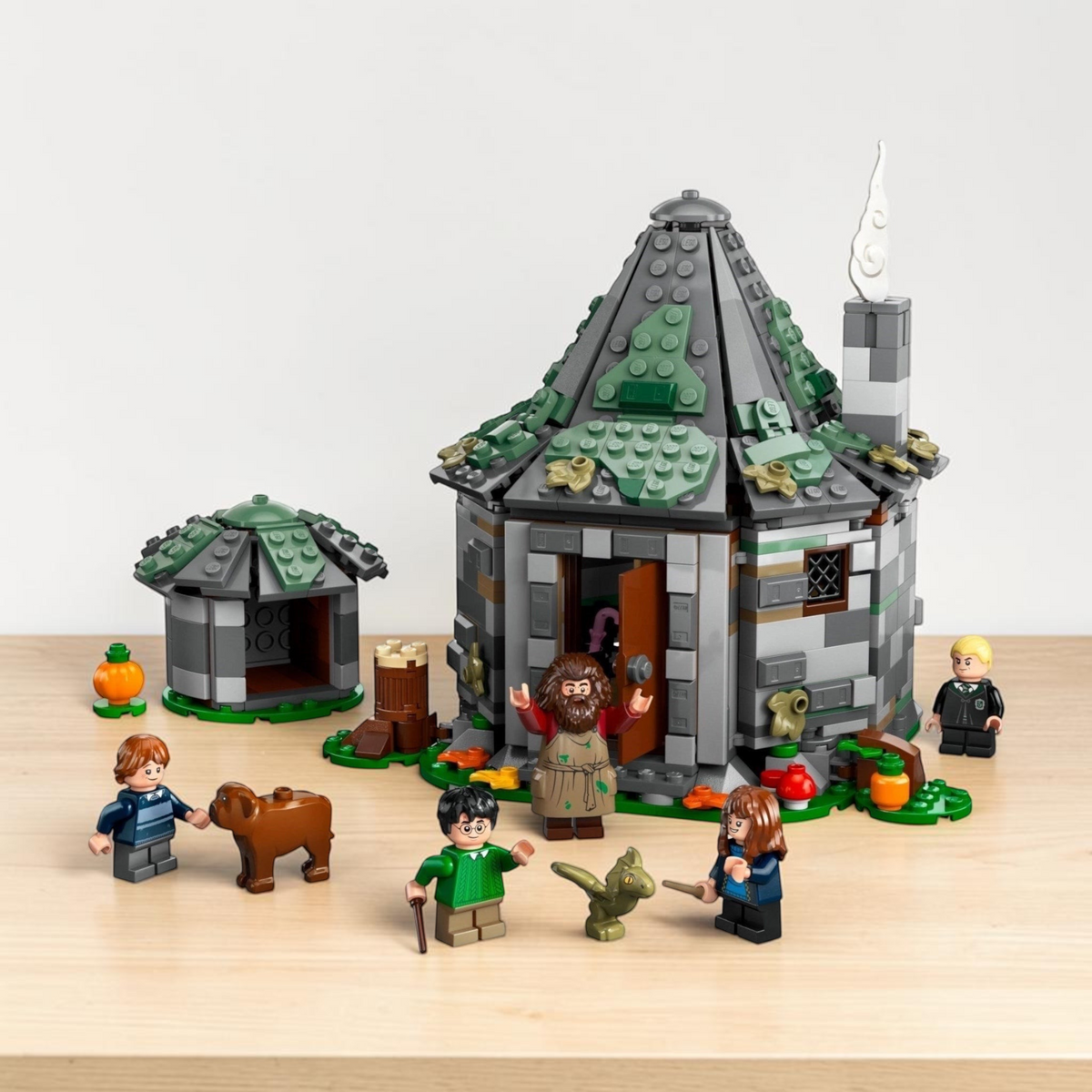[lifestyle-shelf-built] A Brick Apart LEGO Harry Potter Hagrid's Hut set with minifigures, Fang the dog, and Norbert the dragon on a table.