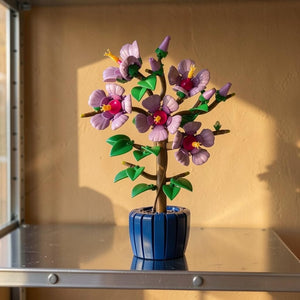 A Brick Apart LEGO Botanicals Hibiscus set featuring lavender flowers with yellow stamens in a dark blue ceramic pot.