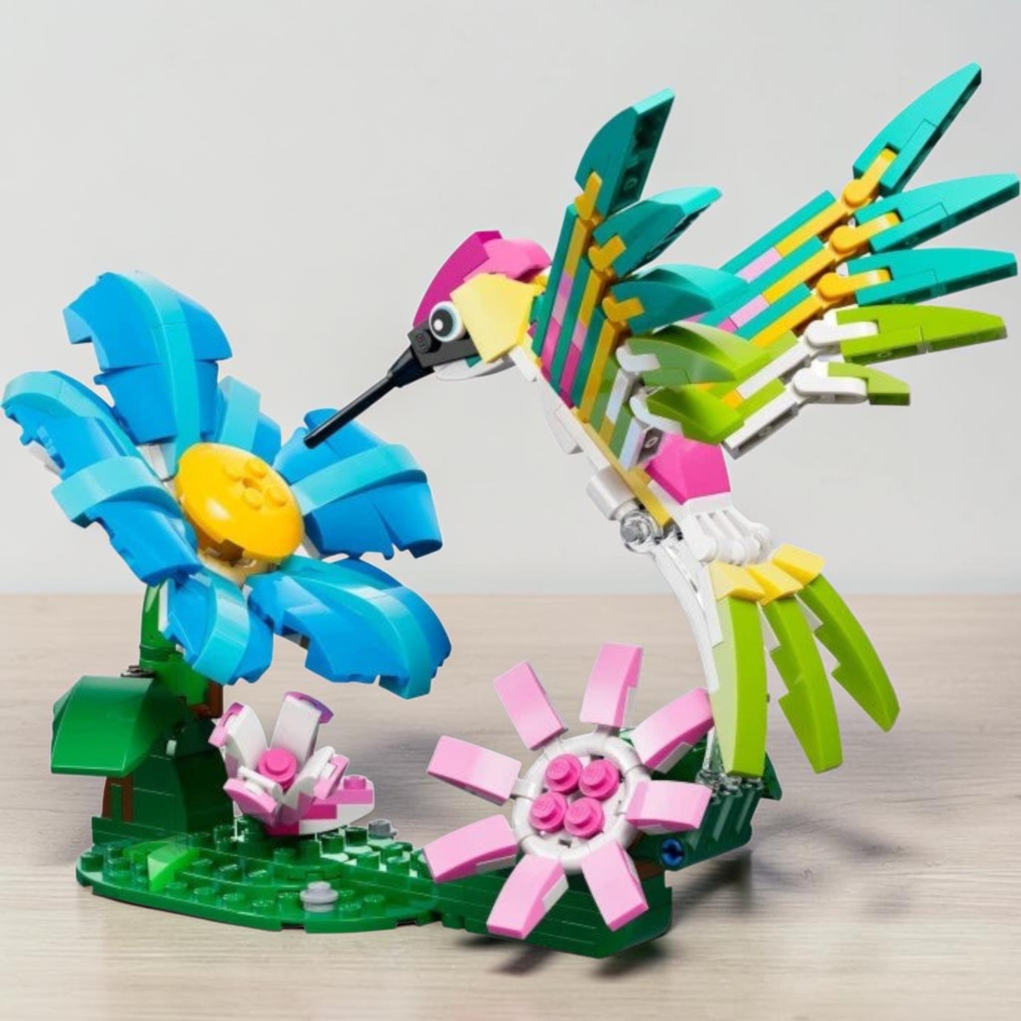 A Brick Apart LEGO Creator colourful hummingbird building set with a posable bird hovering over blue and pink flowers.