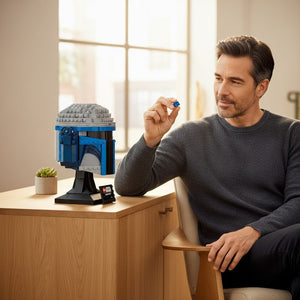 [lifestyle-person] A man building the A Brick Apart LEGO Star Wars Jango Fett Helmet set on a wooden desk with a display stand.