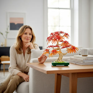 A Brick Apart LEGO Botanicals Japanese Maple Tree set displayed on a wooden table with a woman sitting in the background.