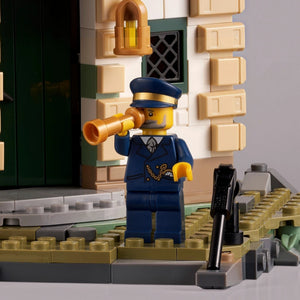 A Brick Apart LEGO Ideas lighthouse keeper minifigure in a blue uniform holding a telescope in front of a stone cottage