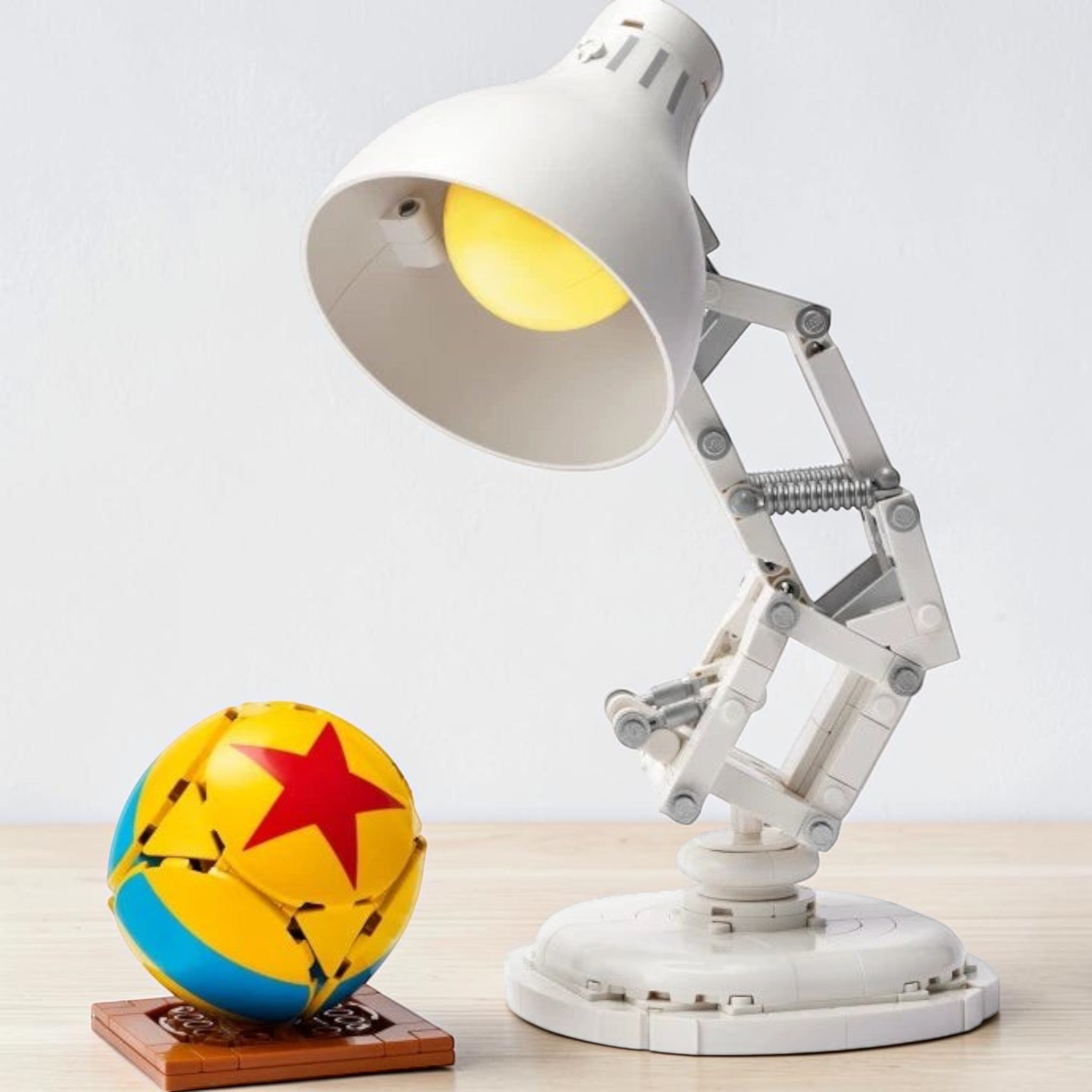 A Brick Apart LEGO Ideas Disney Pixar Luxo Jr. buildable white desk lamp model with a yellow and red Pixar ball.