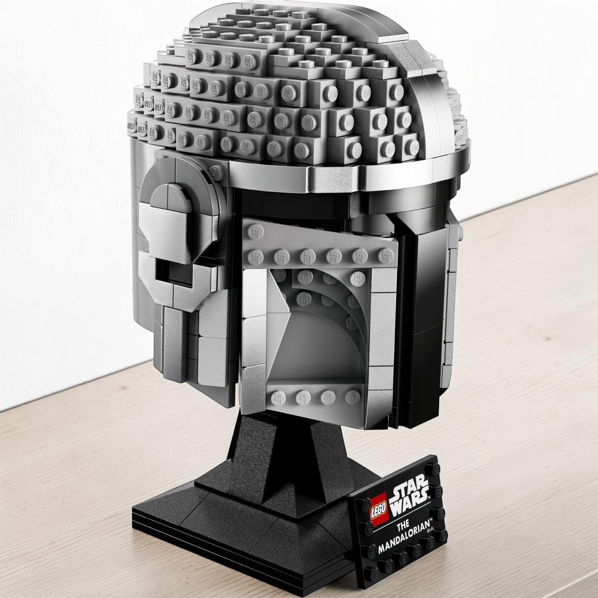 A Brick Apart LEGO Star Wars The Mandalorian helmet model featuring metallic grey beskar armor on a display stand.