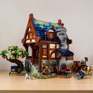 [lifestyle-shelf-built] A Brick Apart LEGO Ideas Medieval Blacksmith set featuring a detailed timber-framed workshop, apple tree, and figures.