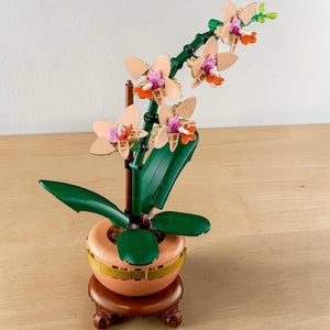 A Brick Apart LEGO Mini Orchid building kit featuring peach flowers, green leaves, and a terracotta pot on a plinth.