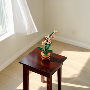 A Brick Apart LEGO Mini Orchid building set featuring peach flowers, green leaves, and a terracotta pot on a plinth.