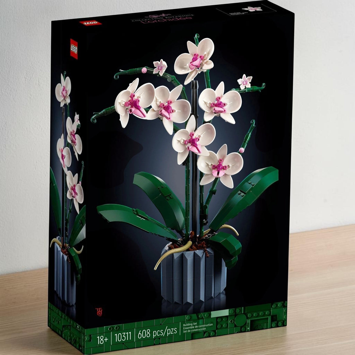 [lifestyle-shelf-box] A Brick Apart LEGO Icons Orchid building set box featuring a white and pink flower model in a blue fluted vase.