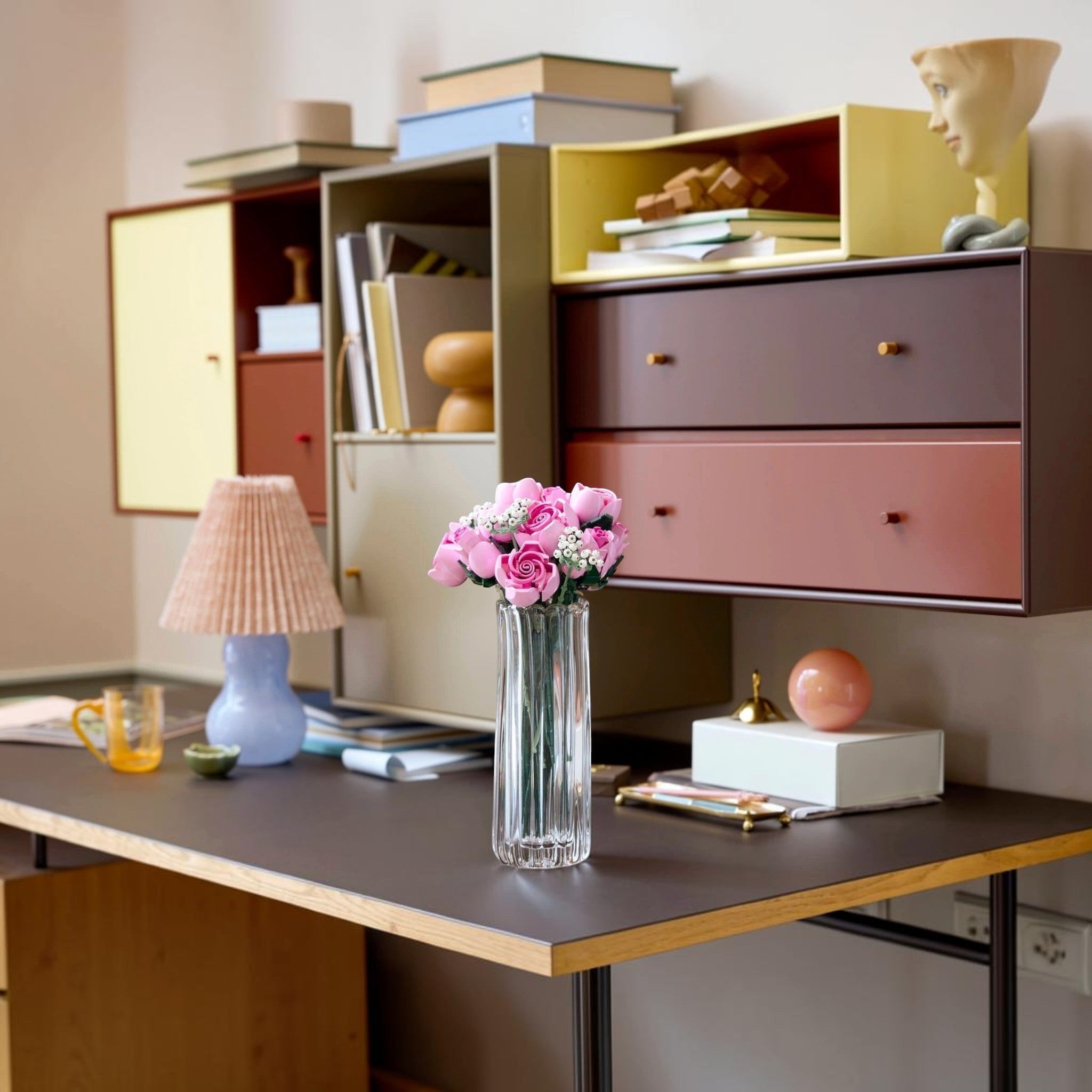 A Brick Apart LEGO Botanicals bouquet of pink roses in a clear glass vase displayed on a modern desk with home decor.