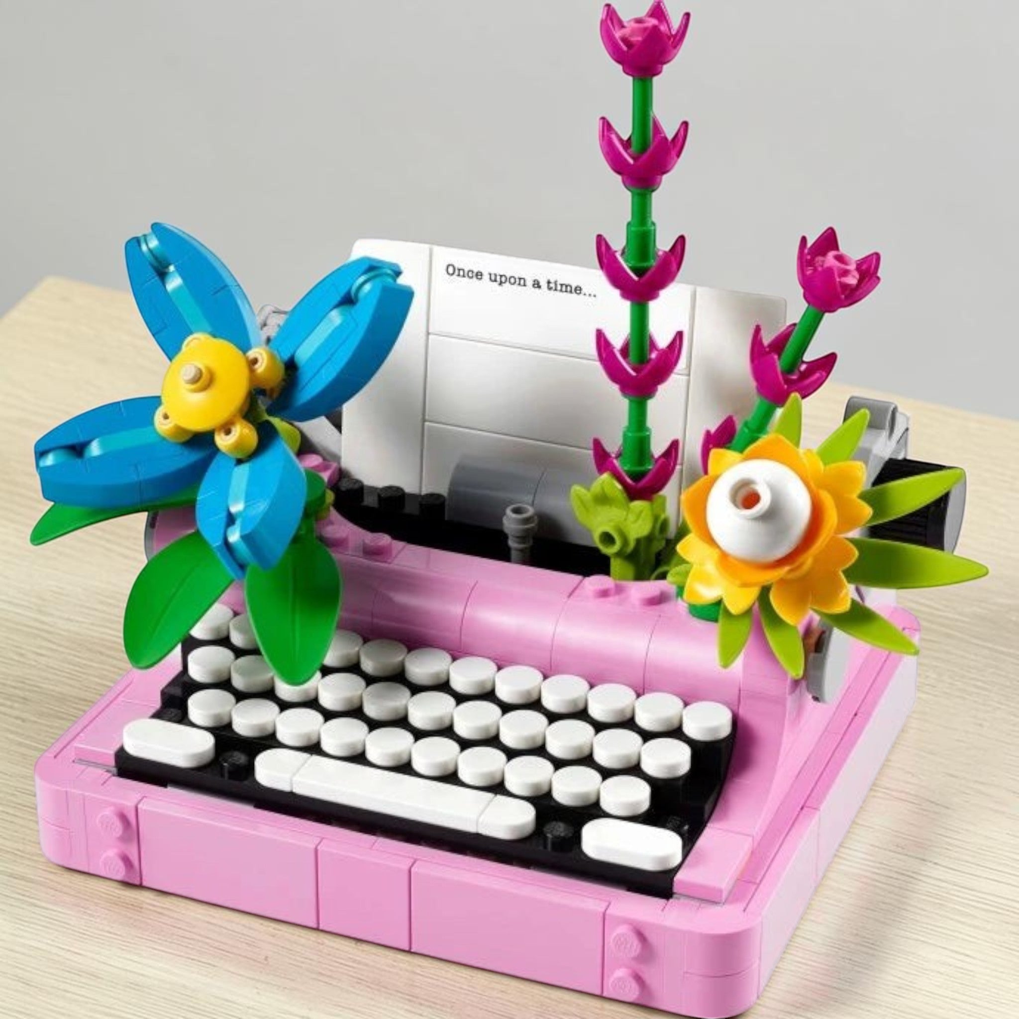 A Brick Apart LEGO Creator typewriter model in pink with colorful brick-built flowers and a paper insert.