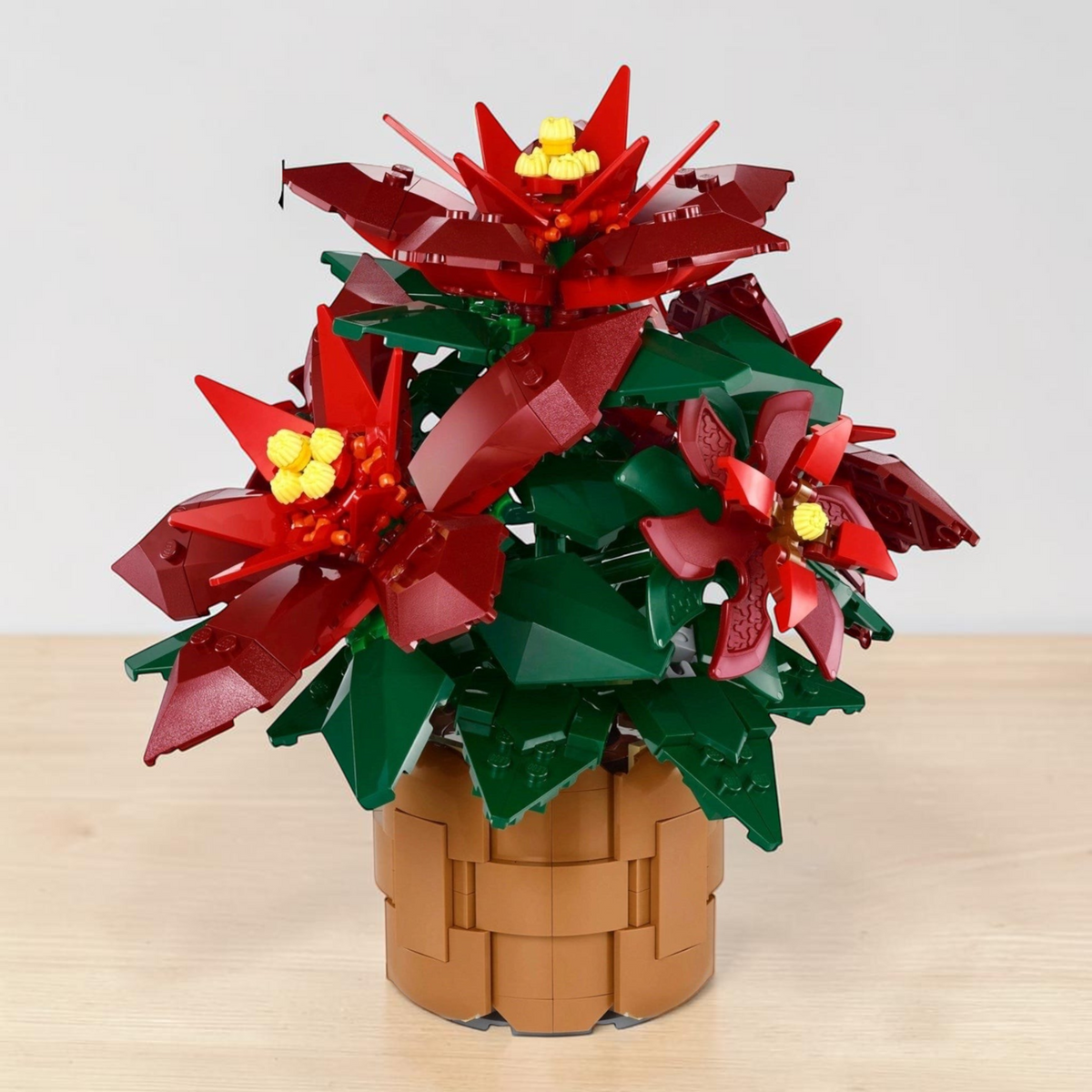 [lifestyle-shelf-built] A Brick Apart LEGO Icons Poinsettia building set featuring vibrant red leaves, green foliage, and a brown woven pot.