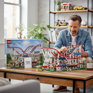 A Brick Apart LEGO Creator Expert Roller Coaster set being assembled by a man at a wooden table with the box nearby.