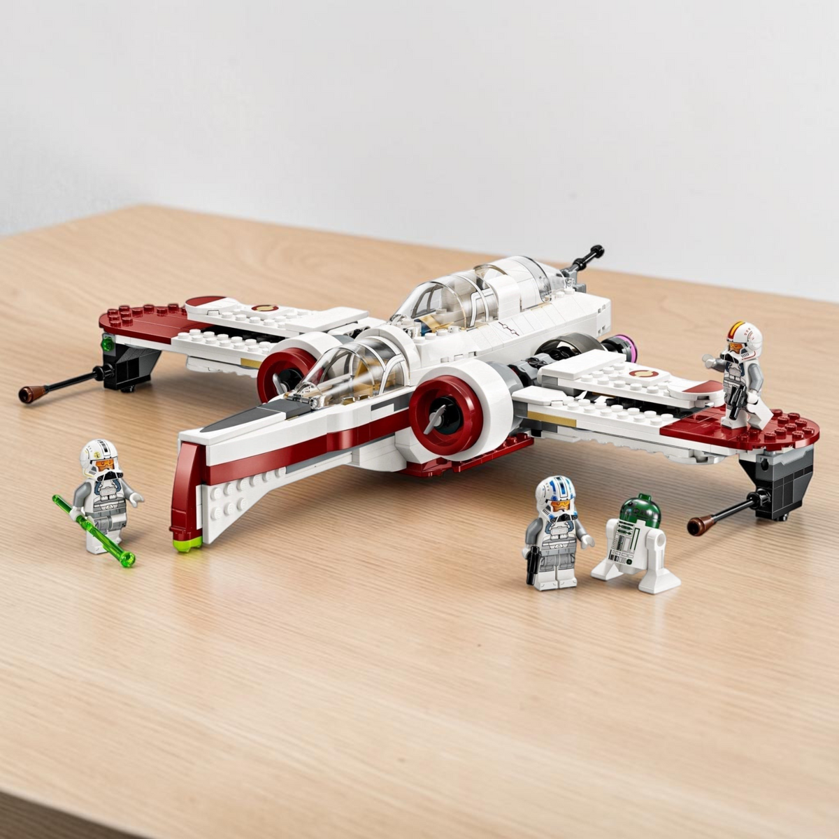 [lifestyle-shelf-built] A Brick Apart LEGO Star Wars ARC-170 Starfighter set with three minifigures and an R4-P44 droid on a wooden table.