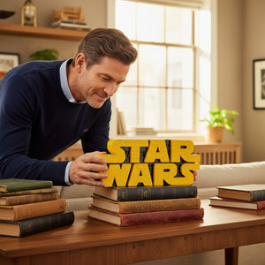 A Brick Apart LEGO Star Wars logo model being placed on a stack of vintage books by a man in a navy sweater.
