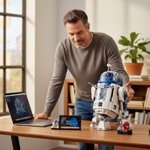 [lifestyle-person] A Brick Apart LEGO Star Wars R2-D2 display model being assembled by a man at a desk with a laptop and information plaque