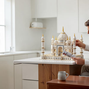 [lifestyle-person] A Brick Apart LEGO Creator Expert Taj Mahal set displayed on a wooden table with a builder holding instructions