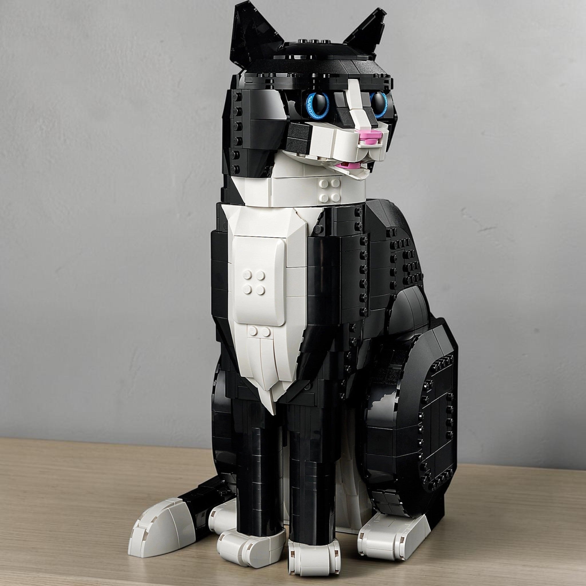 A Brick Apart LEGO Ideas Tuxedo Cat model with black and white bricks, blue eyes, and an open mouth in a sitting pose.