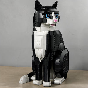 A Brick Apart LEGO Ideas Tuxedo Cat model with black and white bricks, blue eyes, and an open mouth in a sitting pose.