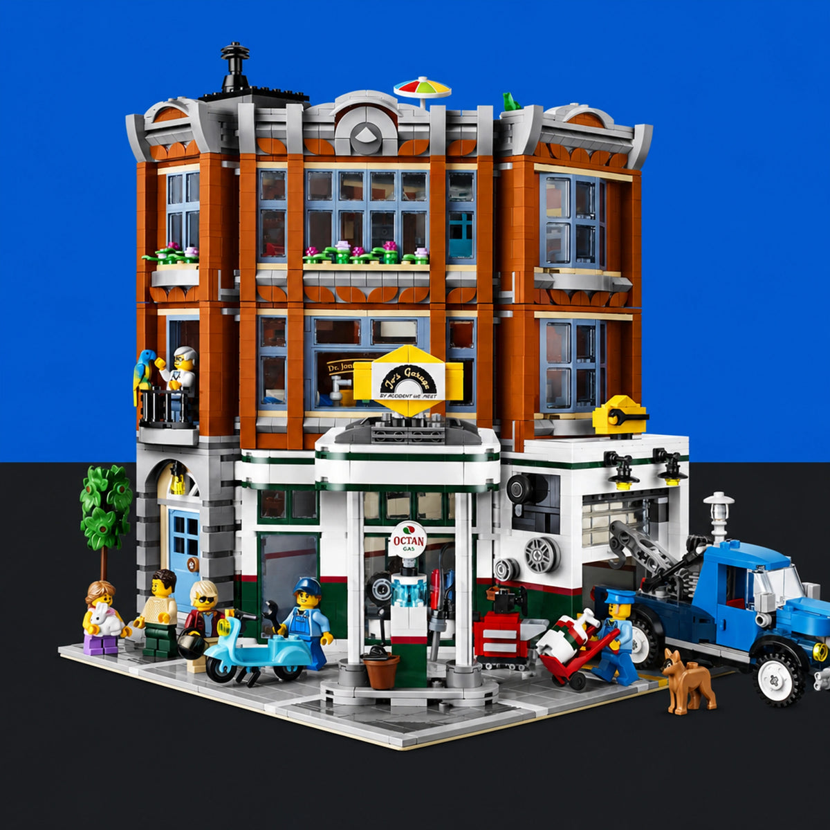 [built-blue-black] A detailed LEGO-style city building set featuring a multi-story brick building with a garage, gas station, and small street scene, shown with minifigures, a blue truck, and a dog against a blue-and-black background.