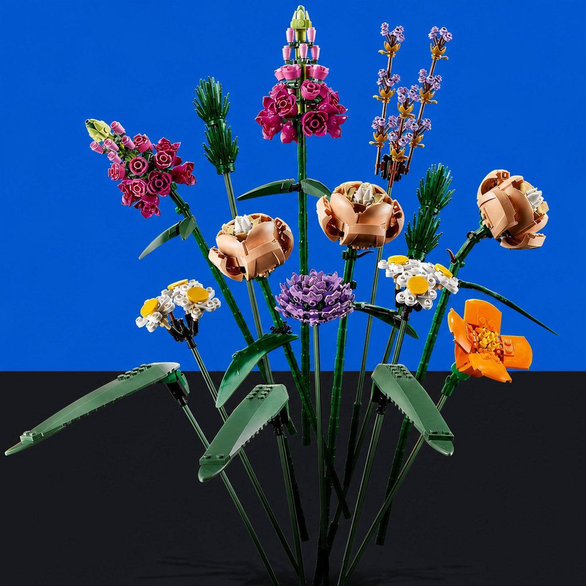 [built-blue-black] A set of assembled toy flowers and leaves arranged like a bouquet on a black surface against a bright blue background. The bouquet includes pink, purple, orange, white, and tan blossoms with green stems and leaves.