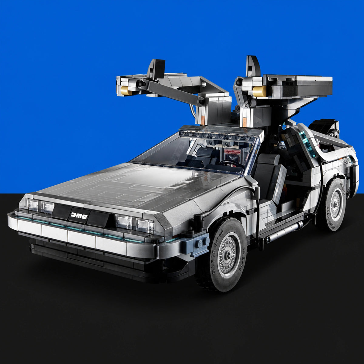 [built-blue-black] A silver and black toy model of a DeLorean time machine from Back to the Future, shown with its gull-wing doors open, set against a solid blue background with a black floor.