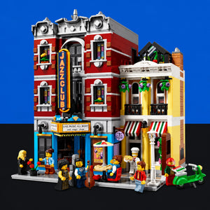 [built-blue-black] A detailed LEGO city building set featuring a red and gray jazz club next to a yellow and white cafe, with minifigures, a green scooter, and small LEGO characters arranged on the street level against a blue and black background.