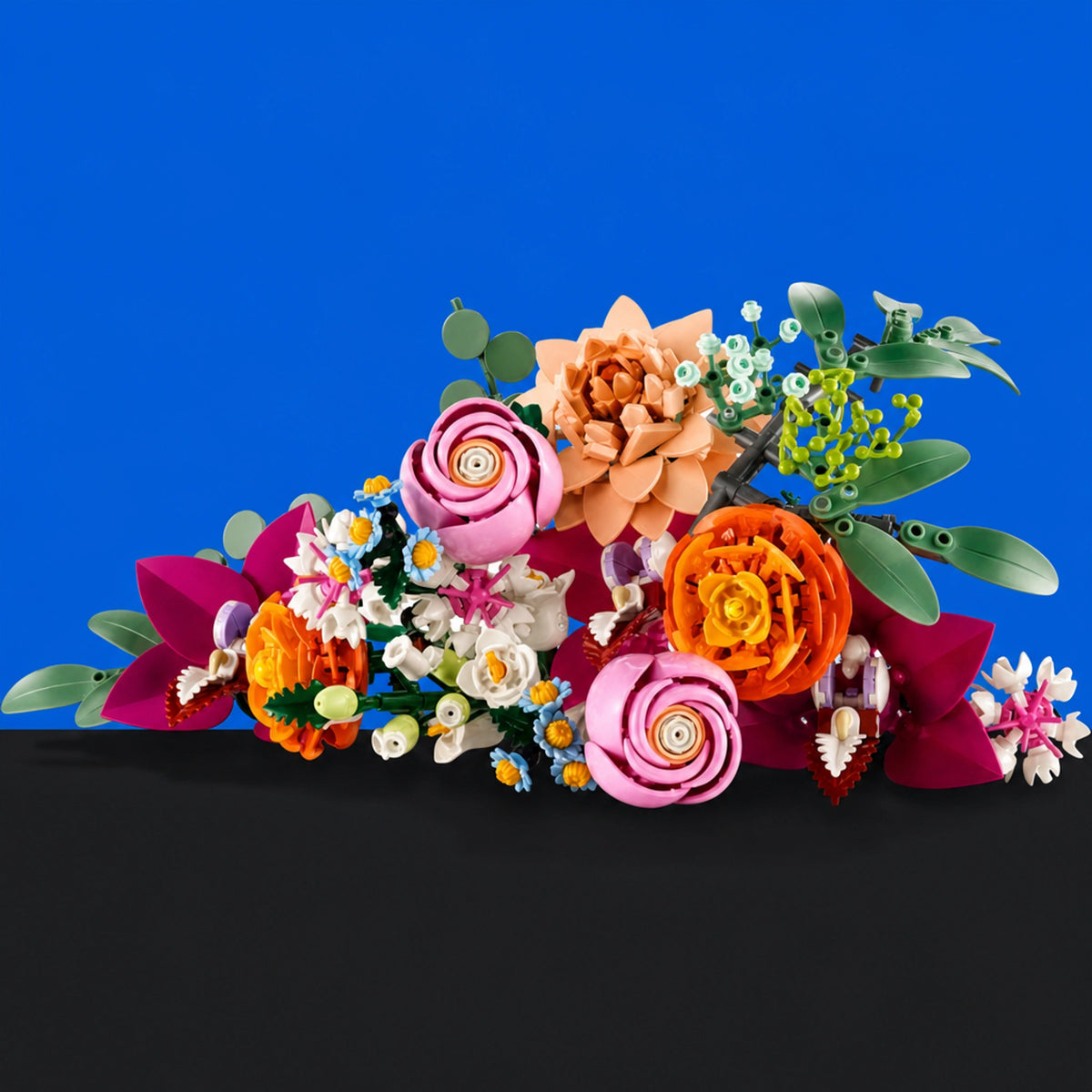[built-blue-black] A colorful arrangement of handmade paper flowers and green leaves, styled on a black surface against a solid blue background.