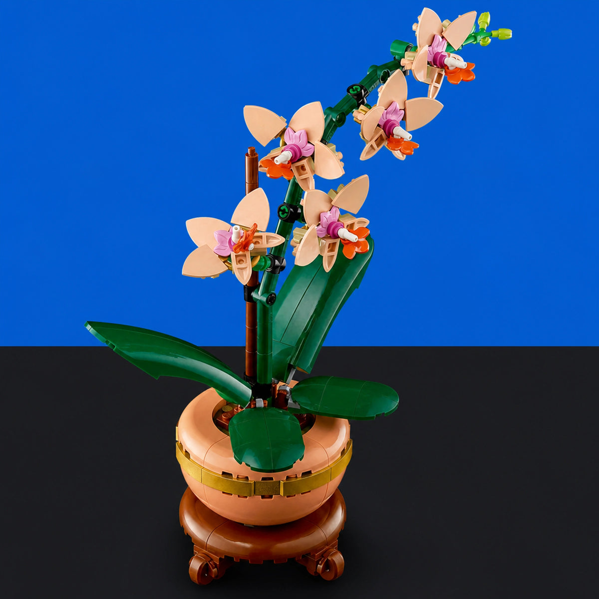 [built-blue-black] A LEGO-style orchid arrangement in a peach-colored pot with green leaves and peach-and-purple flowers, displayed on a wooden stand against a blue and black background.