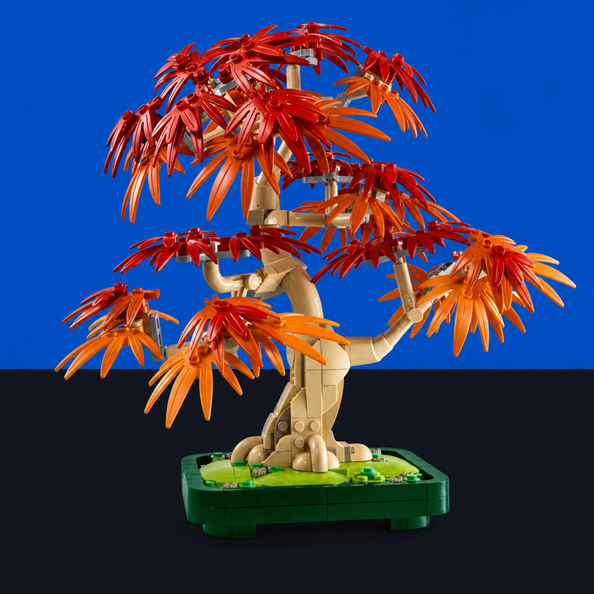 [built-blue-black] A toy bonsai-style tree built from interlocking blocks, with a beige trunk and branches, red and orange leaf pieces, and a green base, photographed against a split blue and black background.