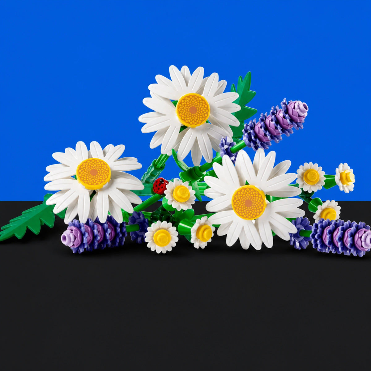 [built-blue-black] A set of building-block style flowers arranged on a black surface against a bright blue background. The bouquet includes large white daisies with yellow centers, smaller white daisies, purple lavender-like spikes, green leaves, and a small red ladybug.